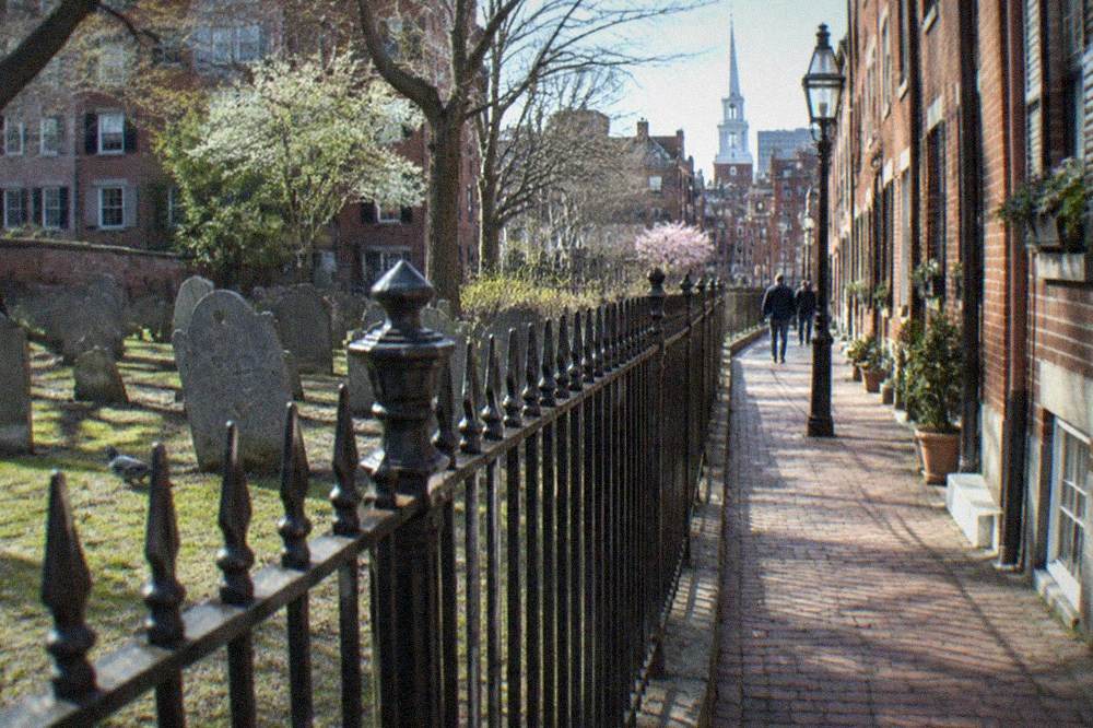 A historic burying ground fence and old brick rowhouses in the North End under clear sky
