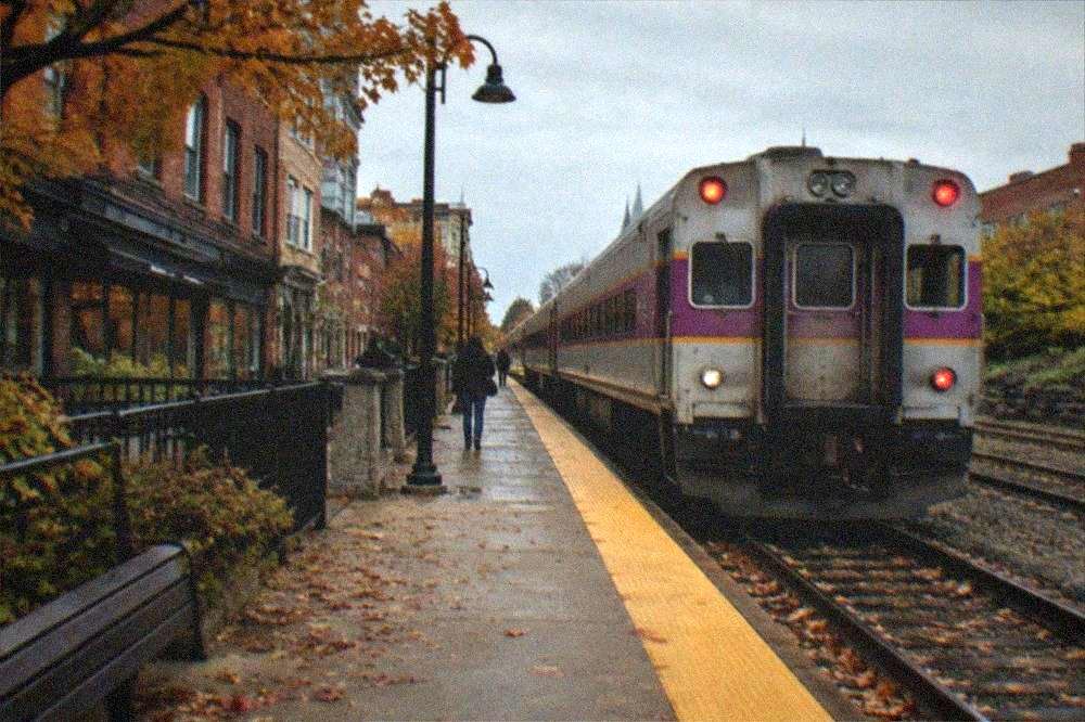 A commuter rail platform with an idling train under a pale autumn sky