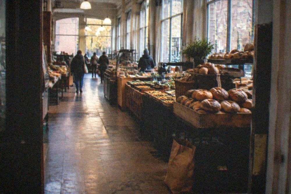 A row of vendor stalls with breads and prepared foods inside a bright indoor public market