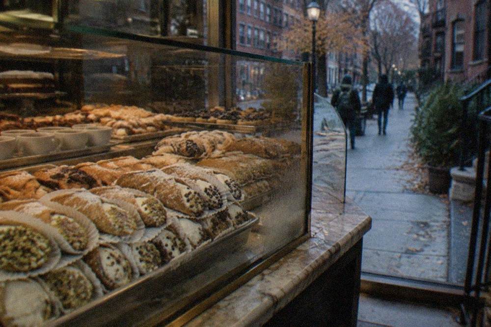 Cannoli arranged in a glass bakery case beside espresso cups on a marble counter