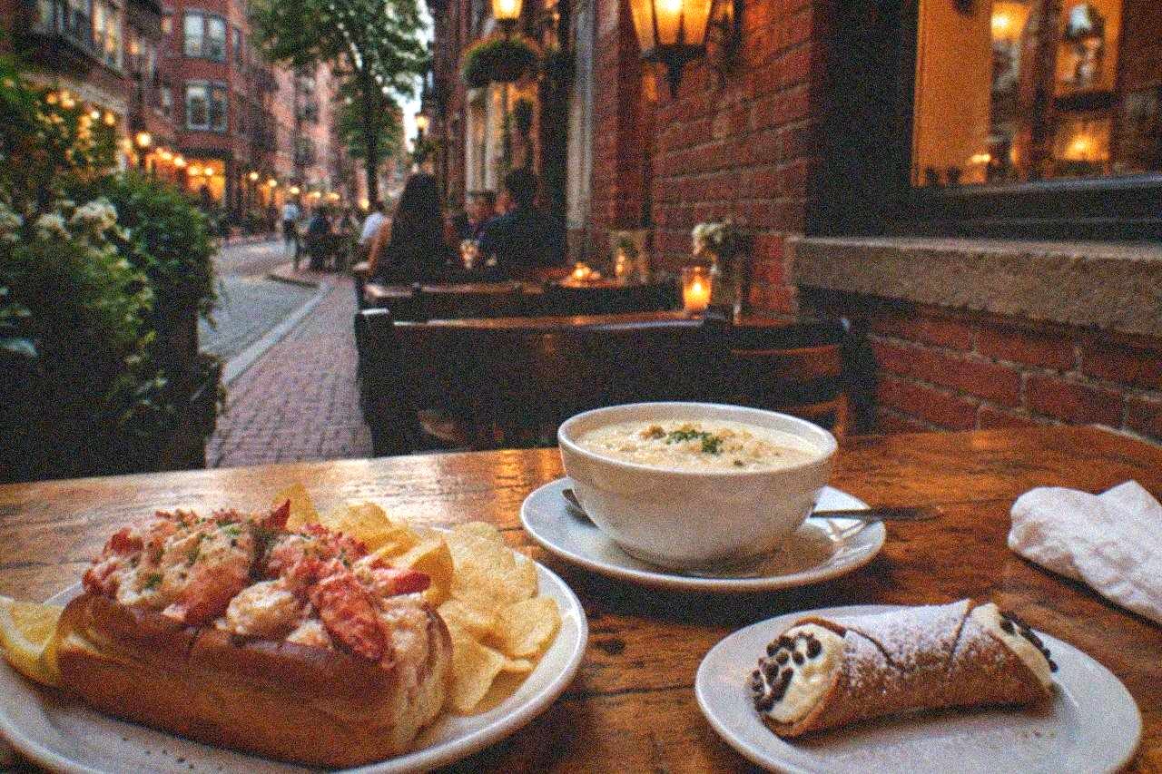 A spread of cannoli, lobster rolls, and clam chowder on a wooden table in a Boston eatery