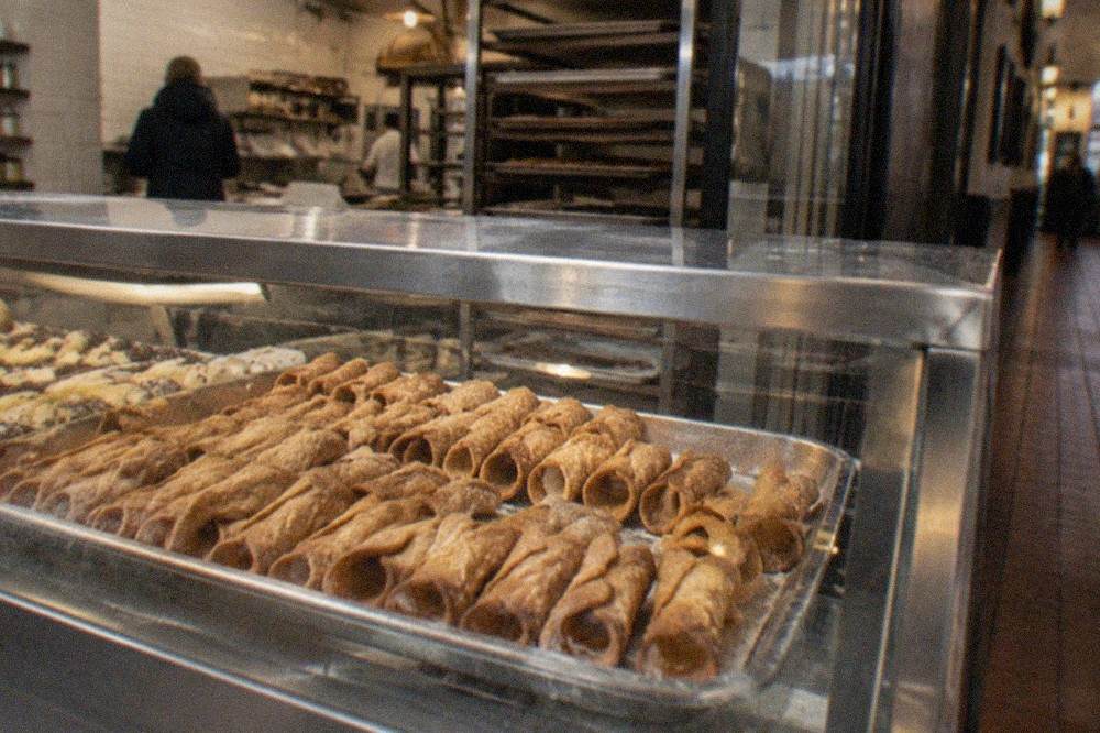 A counter display of freshly baked cannoli arranged in rows inside a small Italian bakery