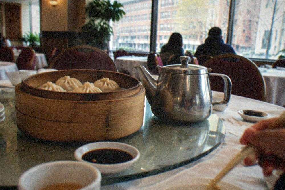 A bamboo steamer basket of dumplings opened on a restaurant table beside a teapot and small dishes