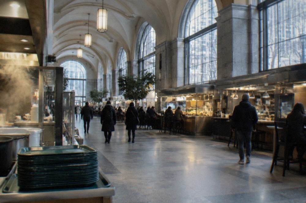 Interior of a long historic food hall with rows of eating stalls beneath high arched windows