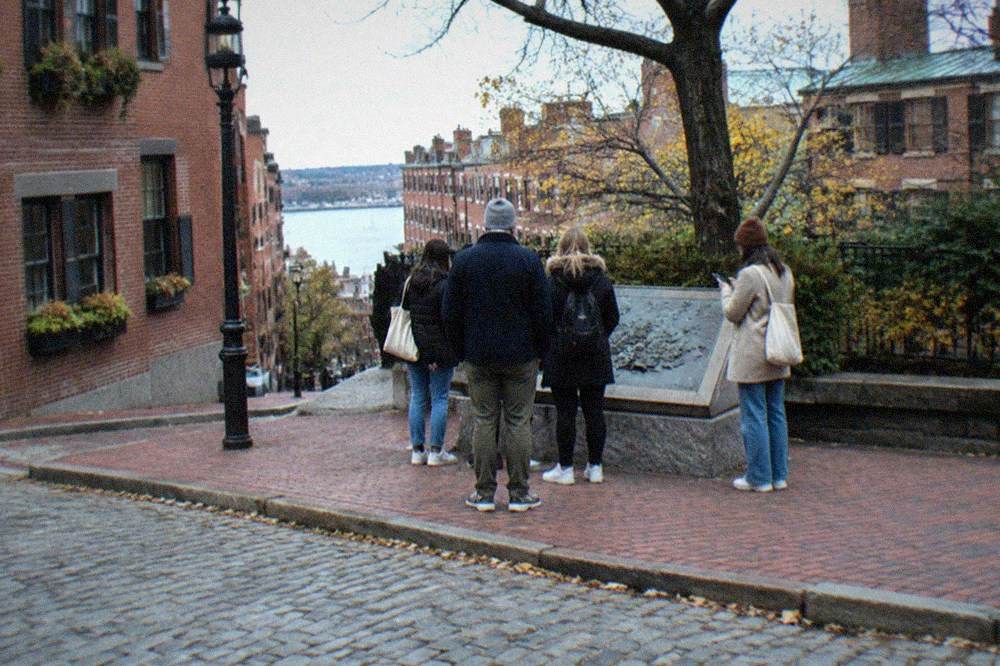 A guided walking group pausing on a brick sidewalk outside a small storefront