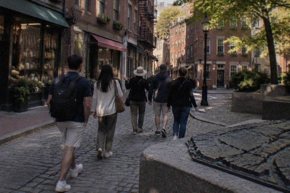 A guide leading a small group past Italian specialty shops on a narrow North End sidewalk