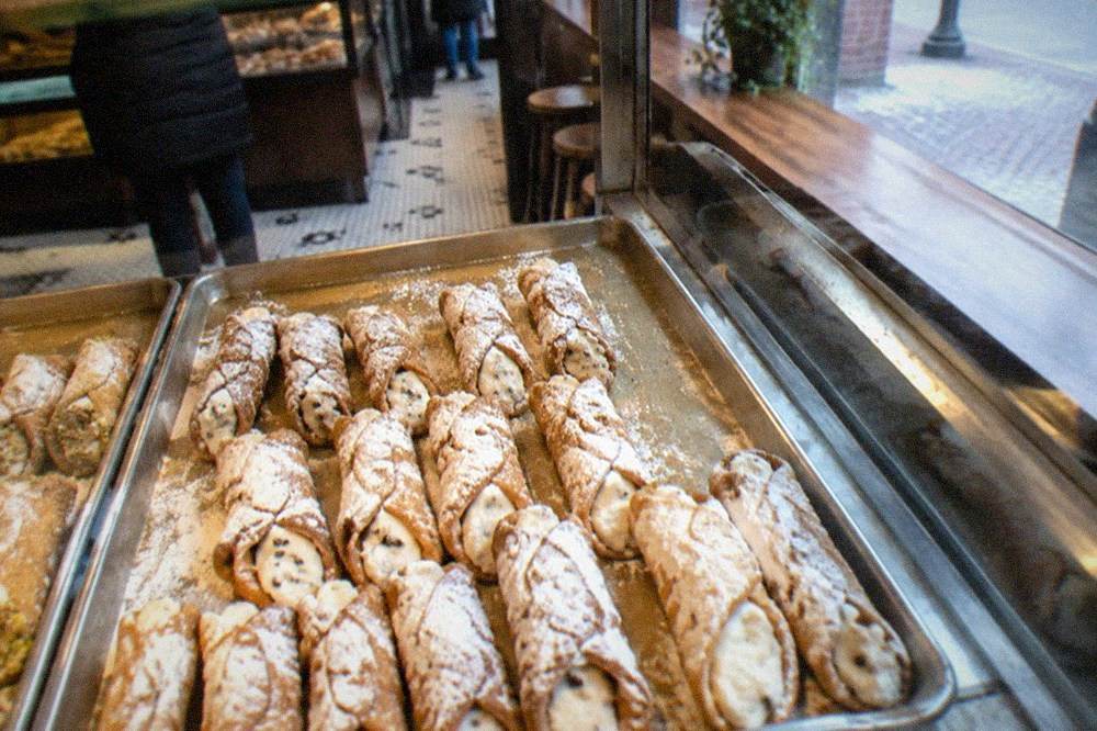 A bakery counter with trays of cannoli arranged behind a glass display case