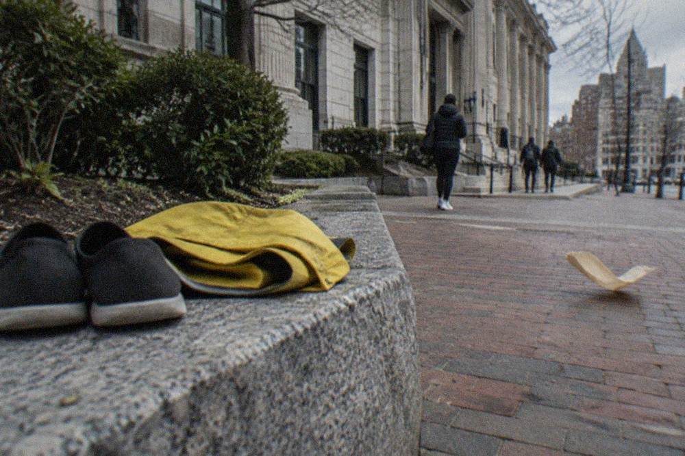 Flat walking shoes resting beside a folded rain jacket on a wooden bench near a brick storefront