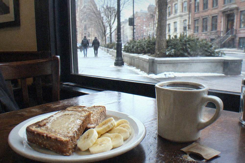 A light morning snack of toast, fruit, and coffee on a small cafe table beside a window