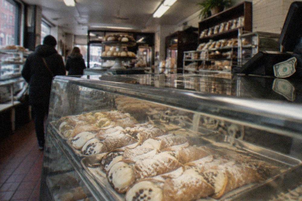 Glass pastry case filled with cannoli dusted with powdered sugar