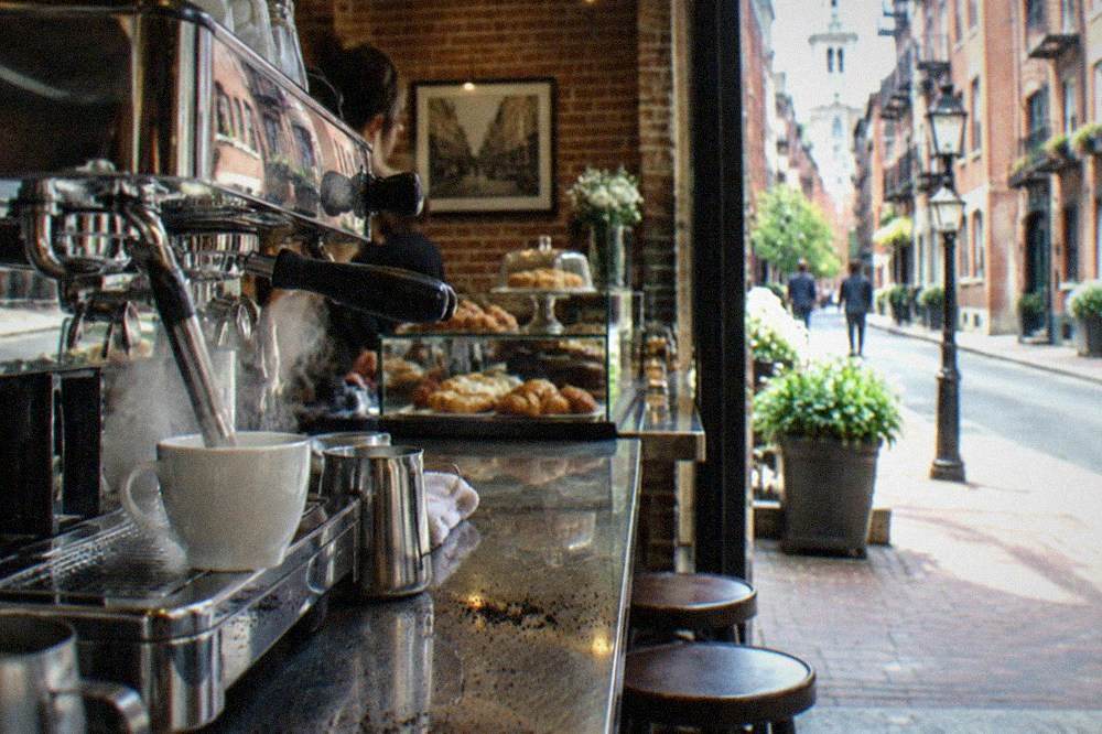 Cafe counter with an espresso machine and glass pastry display in a brick-walled shop