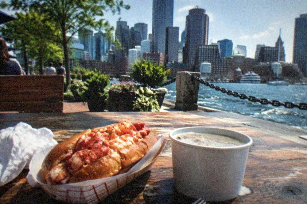 Lobster roll and clam chowder served on a wooden table at a waterfront counter