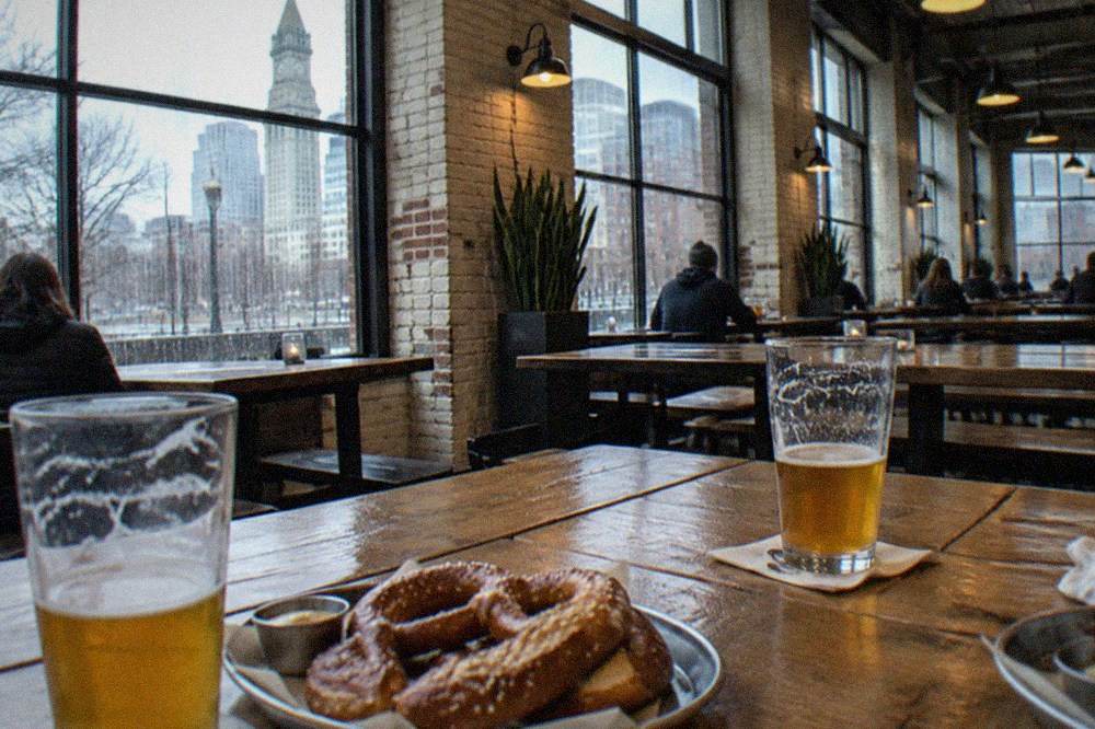 Beer hall tables with pretzels and pint glasses beside brewery windows