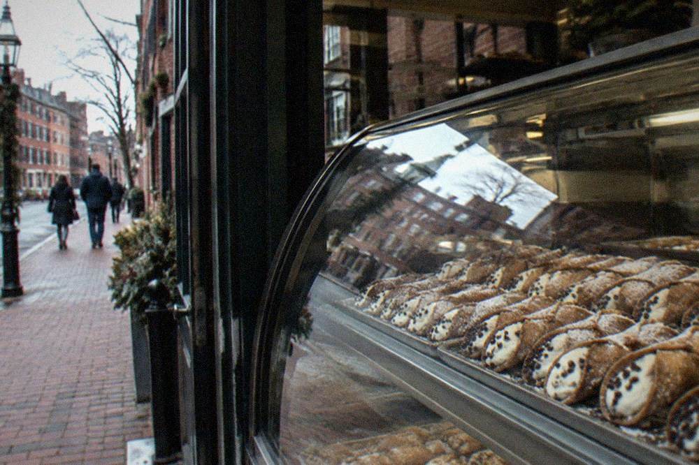 Rows of filled cannoli behind the glass case of a North End pastry shop