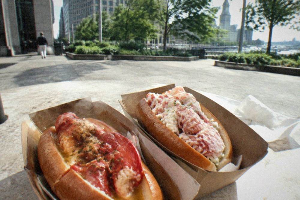 Two lobster rolls side by side, one with warm buttered meat and one with cold lobster salad in a toasted bun