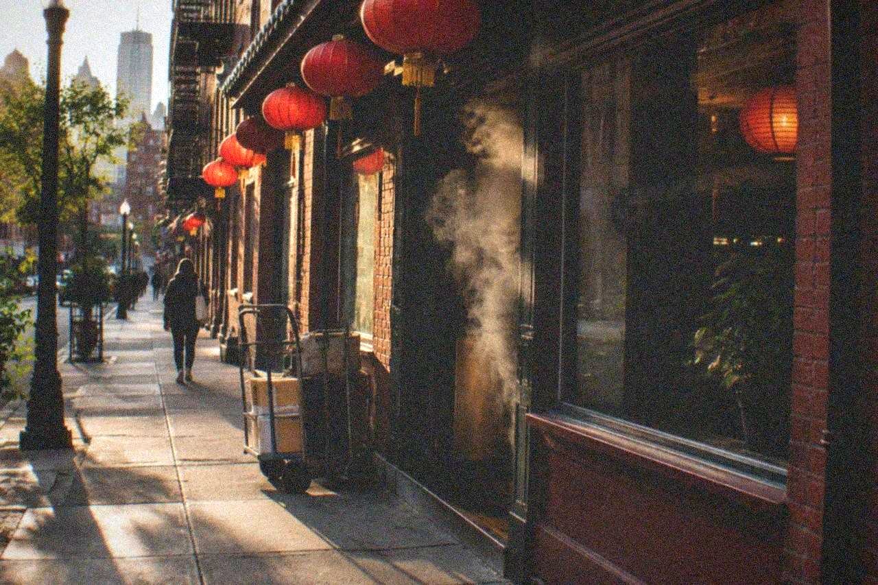 Storefronts with bilingual signs along a narrow Boston Chinatown street in the late afternoon