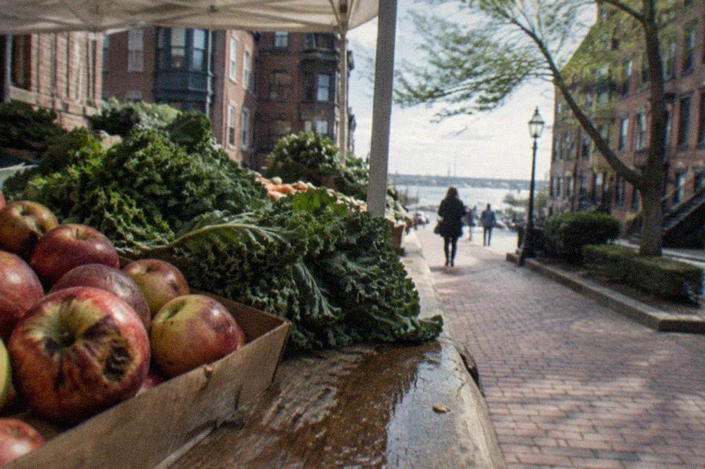 Outdoor produce stalls piled with fruit and vegetables under an awning on a narrow city street