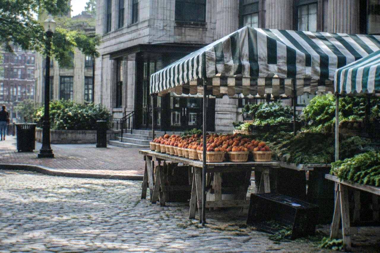 Outdoor produce market stalls with awnings and stacked fresh fruit beside a historic Boston street