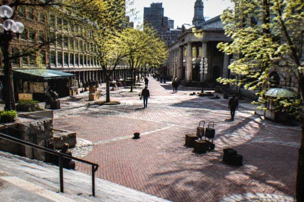 Market plaza between old brick and granite buildings with a clock tower in daylight