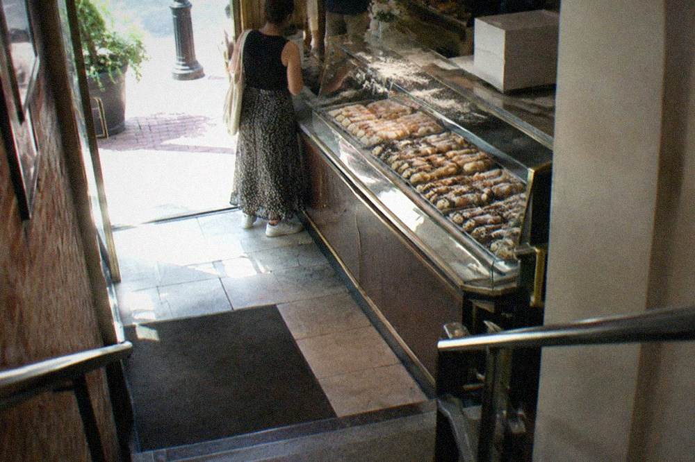 Row of cannoli filled with cream and dusted with powdered sugar in a bakery case