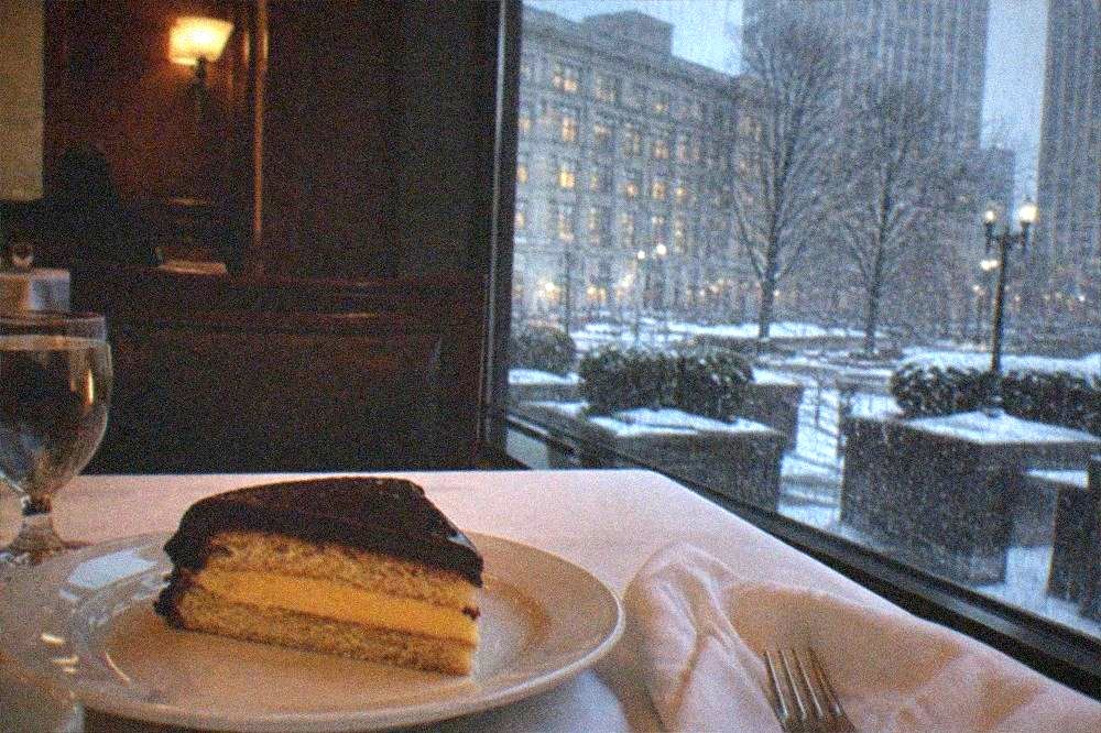 Sponge cake slice with custard filling and chocolate glaze on a white plate