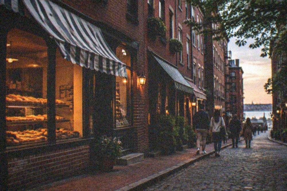 Diners walking a narrow brick street past Italian bakery storefronts with awnings